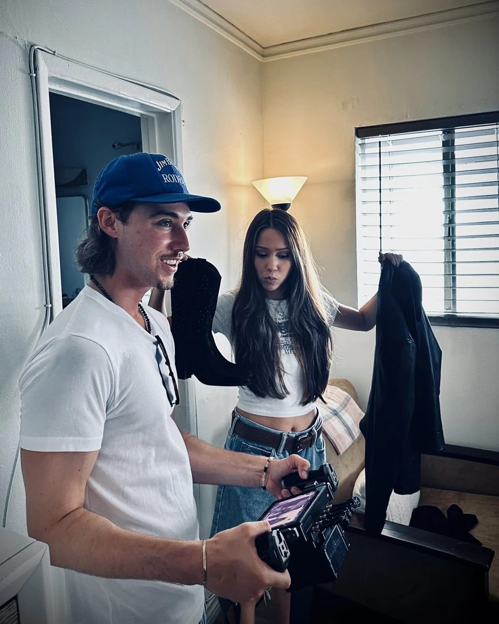 Will Jandro holding a camera rig and smiling on the set of Own Your Look, with the actress holding up a boot and a leather jacket behind him